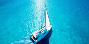 White catamaran sailing on clear blue Aegean Sea with Greek islands.