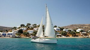 Sailboat on turquoise water near Greek island village.