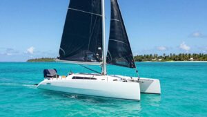 Catamaran sailing on clear blue water near an island.