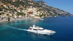 Luxury yacht sailing Italian coast with cliffs and villages.