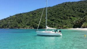 Sailboat anchored in calm, clear water near shore.