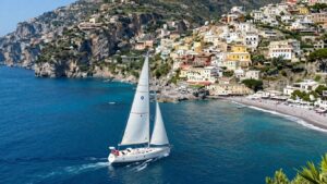 Sailboat on the Italian coast with cliffs and villages.